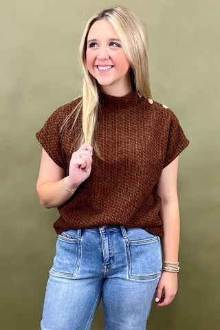 Woman wearing a brown sweater and blue jeans against a green background