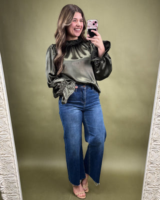 Woman taking a mirror selfie wearing a green tie-dye shirt and blue jeans on a green background.