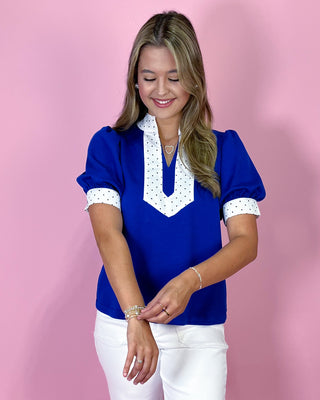 Woman wearing a blue blouse with white polka dot details on a pink background