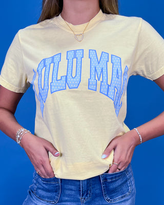 A woman posing in a light yellow graphic t-shirt with blue lettering, paired with blue jeans