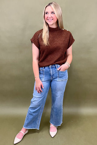 Woman wearing a brown top and blue jeans against a green background
