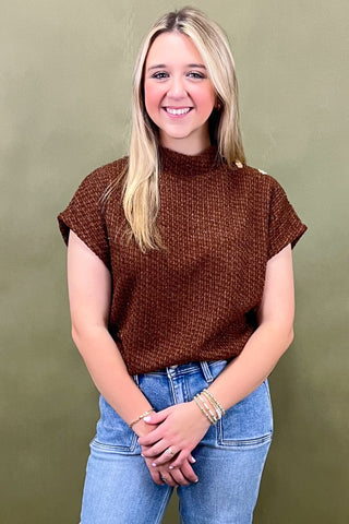 Woman wearing a brown textured top and blue jeans against a green background