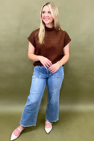 Woman wearing a brown top and blue jeans against a green background
