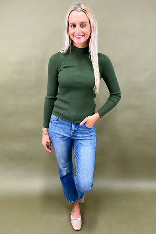 Woman wearing a green ribbed sweater and blue jeans on a beige background
