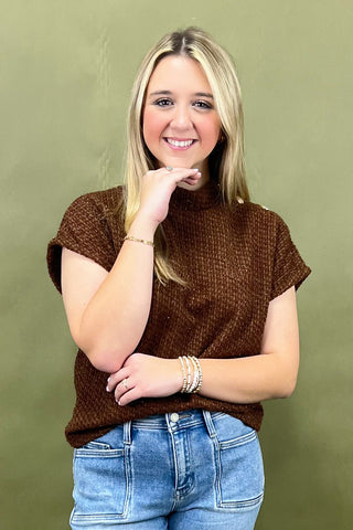 Woman wearing a brown knitted top and blue jeans against a green background