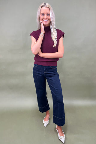 Woman wearing a burgundy top and blue jeans against a plain background