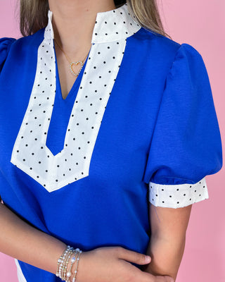 Blue blouse with white polka dot trim on a pink background