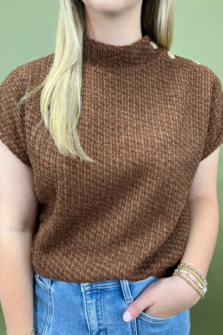 Person wearing a brown knitted sweater and blue jeans against a green background