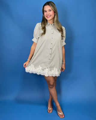 A woman modeling a short-sleeve button-front shirt dress with thin vertical stripes and a lace hem
