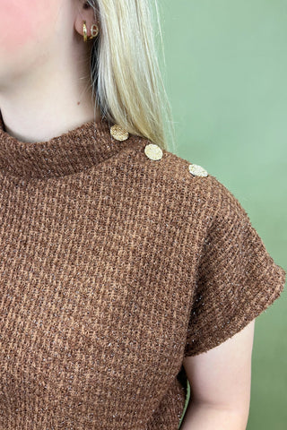 Brown textured sweater with gold buttons on a green background