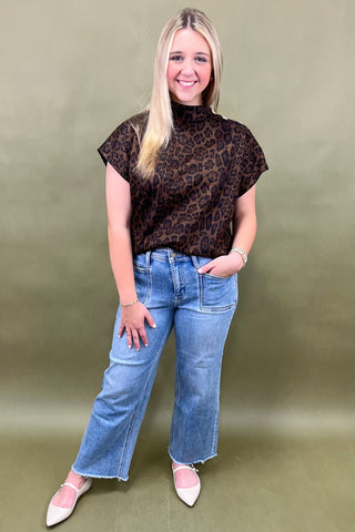 Woman wearing a leopard print top and blue jeans against a green background
