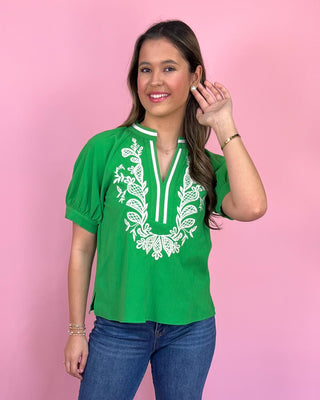 Woman wearing a green blouse with white embroidery against a pink background