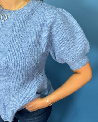 Woman modeling a light blue cable knit puff sleeve peplum sweater top with dark wash wide leg jeans.