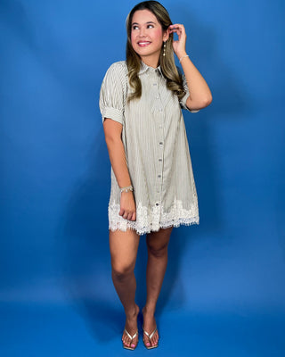 A woman modeling a short-sleeve button-front shirt dress with thin vertical stripes and a lace hem