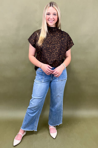 Woman wearing a leopard print top and blue jeans against a green background