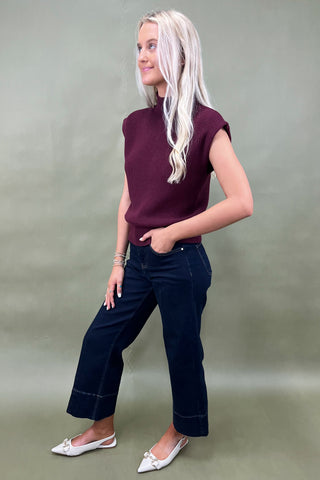 Woman wearing a maroon top and dark blue jeans against a plain background