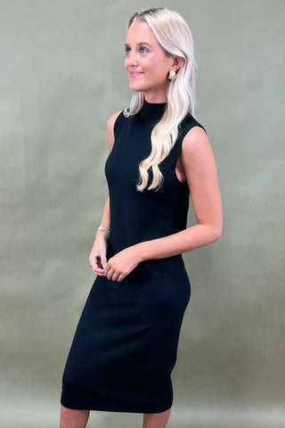 Woman wearing a black sleeveless dress against a plain background