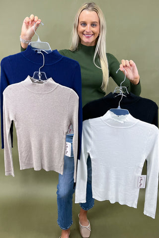 Woman holding three turtleneck sweaters in blue, gray, and white against a green background