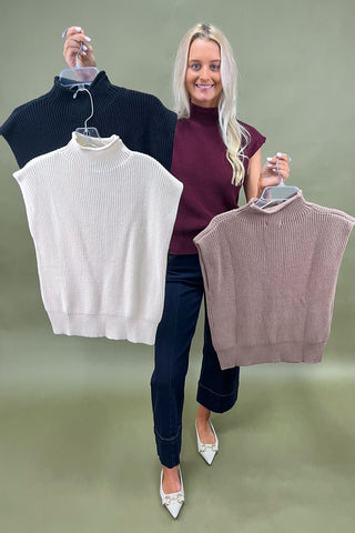 Woman holding three sleeveless sweaters against a green background