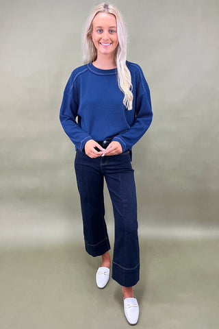 Woman wearing a blue sweater and dark jeans on a plain background