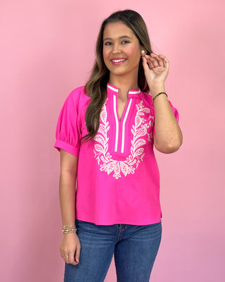 Woman wearing a pink blouse with white lace details against a pink background