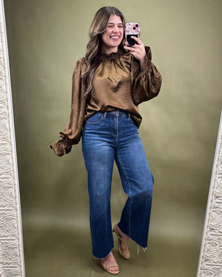 Woman taking a mirror selfie wearing a brown blouse and blue jeans on a green background