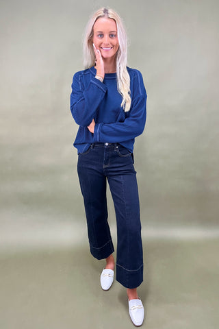 Woman wearing a blue sweater and dark jeans against a plain background