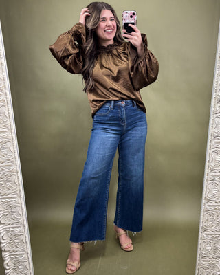 Woman taking a mirror selfie wearing a brown blouse and blue jeans on a green background