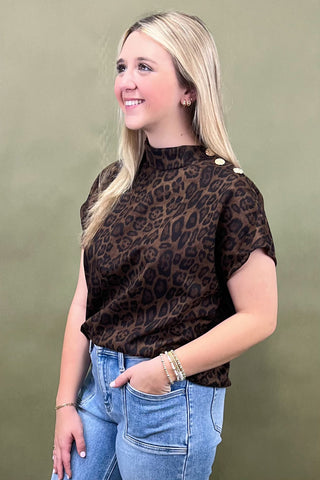 Woman wearing a leopard print top with button details against a green background