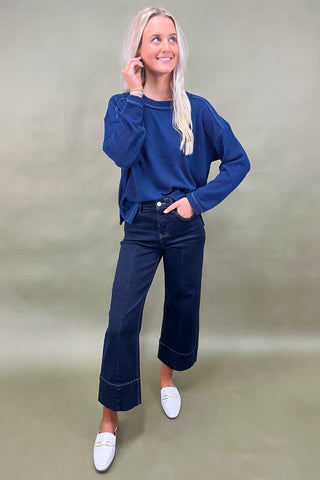 Woman wearing a blue sweater and dark jeans on a plain background