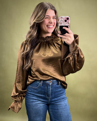 Woman taking a mirror selfie wearing a brown blouse and blue jeans on a green background
