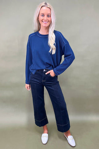 Woman wearing a blue sweater and dark jeans against a plain background