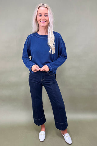 Woman wearing a blue sweater and dark jeans against a plain background