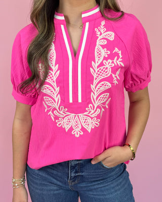 Person wearing a pink blouse with white embroidery against a pink background