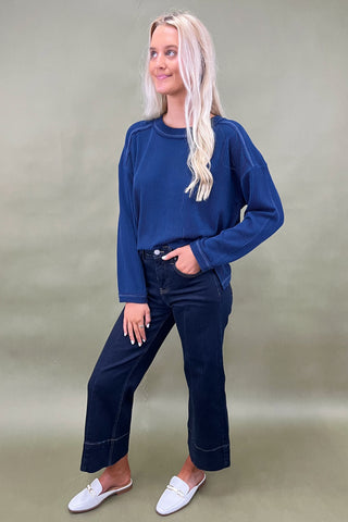 Woman wearing a blue sweater and dark jeans against a plain background