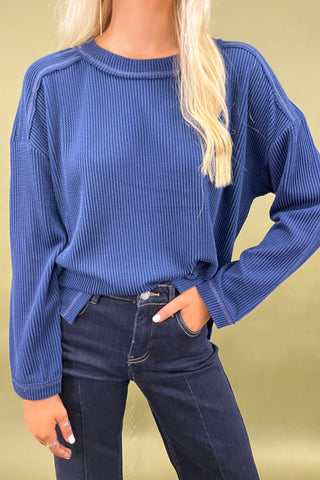 Person wearing a blue ribbed sweater and dark jeans against a beige background
