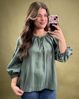 Woman taking a mirror selfie wearing a green blouse against a beige background