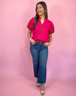 Woman wearing a pink blouse with lace sleeves and blue jeans against a pink background