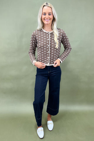Woman wearing a patterned blouse and dark pants against a plain background