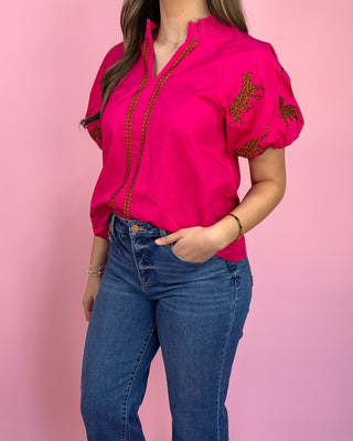 Person wearing a pink blouse with red embroidery and blue jeans on a pink background