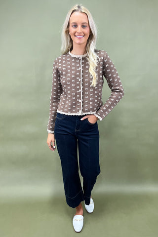 Woman wearing a patterned blouse and dark pants against a plain background