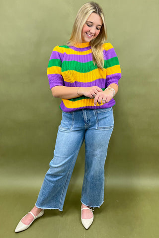 Woman wearing a colorful striped sweater and blue jeans on a green background