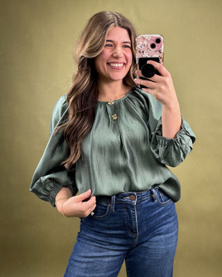 Woman taking a selfie wearing a green blouse and blue jeans on a gold background