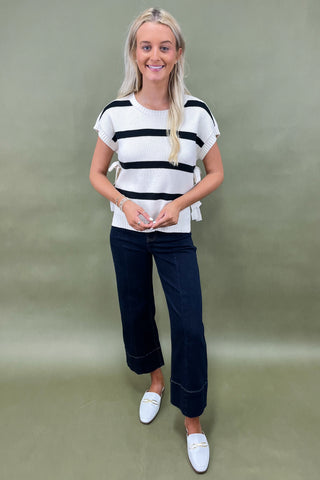 White knit top with black horizontal stripes and side bow detail styled with dark wide leg cropped jeans and white loafers