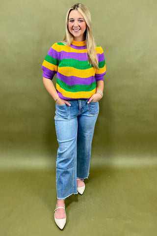 Person wearing a colorful striped sweater and jeans on a green background