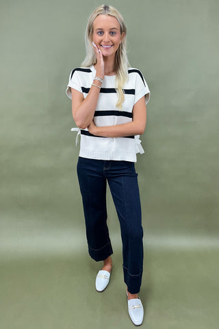White knit top with black horizontal stripes and side bow detail styled with dark wide leg cropped jeans and white loafers