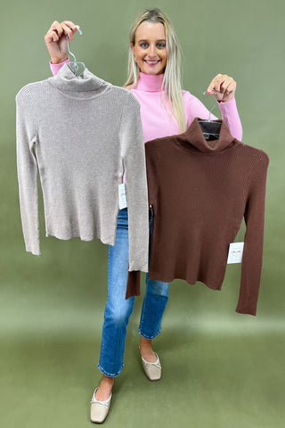 Woman holding two sweaters, one gray and one brown, against a green background