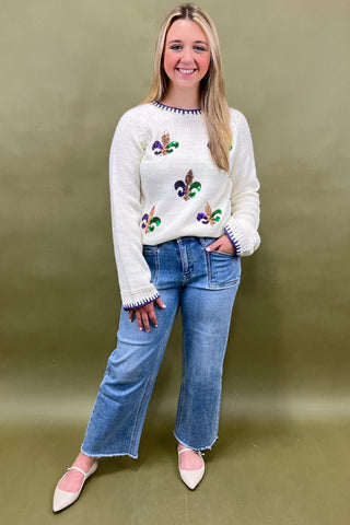 Woman wearing a white sweater with floral patterns and blue jeans on a green background