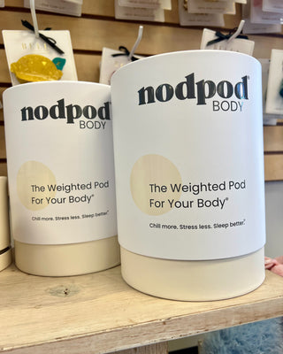 Two 'nodpod BODY' weighted pods on a shelf in a store setting.