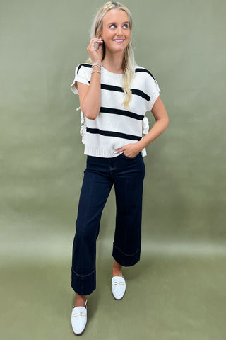 White knit top with black horizontal stripes and side bow detail styled with dark wide leg cropped jeans and white loafers